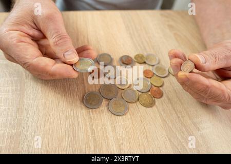 Un anziano, povero pensionato, mette monete da centesimo euro su tavola di legno, conta poco denaro contante sul tavolo, illustrando la dura realtà della vita in povertà Foto Stock