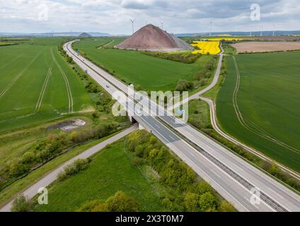 Wolferstedt, Germania. 26 aprile 2024. L'Autobahn 38 si snoda attraverso il paesaggio del distretto di Mansfeld-Südharz tra le macchie di scorie dell'ex miniera di rame. Tra il 2020 e il 2040, si prevede che la popolazione di Mansfeld-Südharz diminuirà del 21,1%. Previsioni analoghe sono formulate per gli altri stati della Germania orientale. Allo stesso tempo, la percentuale di anziani è in aumento. I distretti stanno facendo del loro meglio per combattere questa situazione. (Vista aerea con drone) credito: Jan Woitas/dpa/Alamy Live News Foto Stock