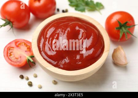 Delizioso ketchup nel recipiente, aglio e pomodori su un tavolo di legno bianco, primo piano Foto Stock