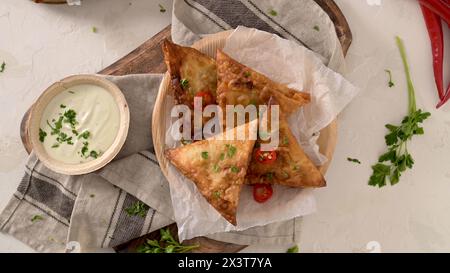 Samosa indiana - pasticceria fritta o al forno con ripieno salato, popolari spuntini indiani, servita in piatti a foglia areca con spezie sul banco della cucina. Foto Stock