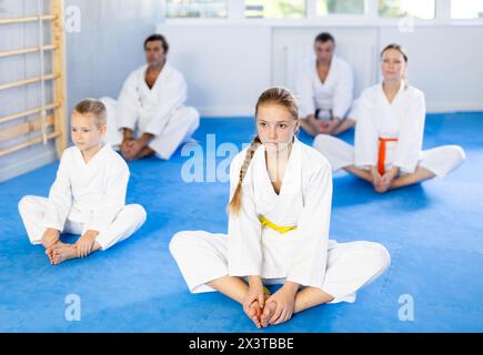 La famiglia durante l'allenamento di gruppo di karate con l'allenatore in palestra esegue lo stretching dei muscoli eseguendo l'esercizio di farfalla Foto Stock