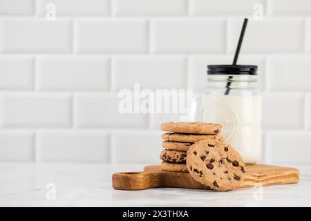 I biscotti vengono spalmati su un piatto, un bicchiere di latte fresco. Biscotti fatti in casa con gocce di cioccolato. Foto Stock