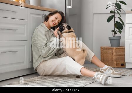 Giovane donna con un carino cane seduto sul pavimento in cucina Foto Stock