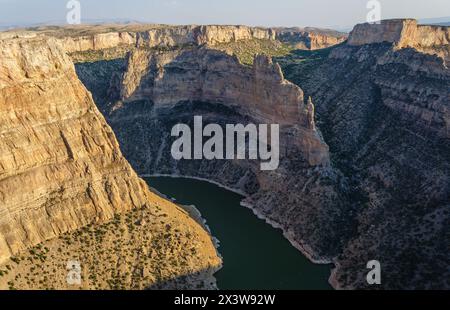 Una veduta di un profondo canyon mostra scogliere beige stratificate che scendono verso un'ansa di fiume verde scuro nella luce della sera presso la Bighorn Canyon National Recreation Area. Foto Stock