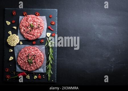 Vista dall'alto delle cotolette di hamburger crude tritate pronte per la cottura con ramoscello rosematoso, aglio e peperoncino su una tavola di ardesia, cottura in background Foto Stock
