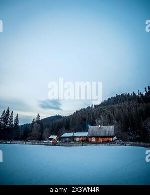 Cottage rurale in legno sulle montagne di sera. Capanna in legno su colline con vecchia recinzione Foto Stock