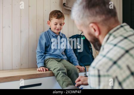 Padre che aiuta figlio a prepararsi per l'asilo, asilo. Pantalone, scarpe, cestino per il pranzo con spuntini. Foto Stock