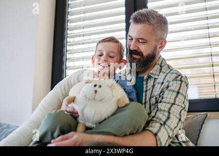 Ritratto di un ragazzo sorridente con il padre, che tiene in mano il suo peluche preferito. Foto Stock