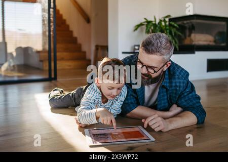 Padre che mostra al figlio un sistema di casa intelligente, che regola le funzioni domestiche, l'illuminazione, le telecamere di sicurezza, le serrature delle portiere e le impostazioni del termostato o del riscaldamento intelligenti Foto Stock