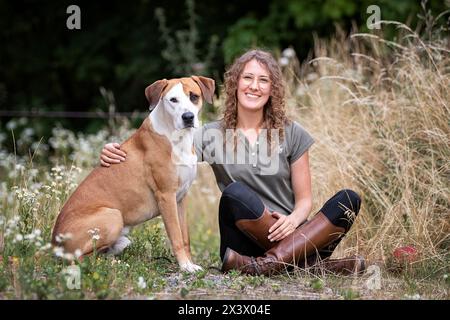 Donna seduta accanto a un cane di razza mista (Boxer x ?). Germania Foto Stock