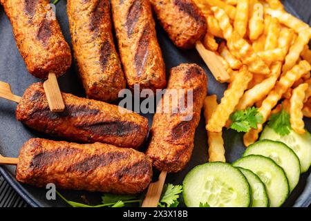 Soutzoukakia greco alla griglia, spiedini di manzo macinato con patatine fritte, cetriolo sul piatto, primo piano Foto Stock