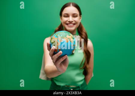 Una giovane donna di vent'anni tiene delicatamente un piccolo globo nelle sue mani, simboleggiando la cura, l'unità e la connessione globale. Foto Stock