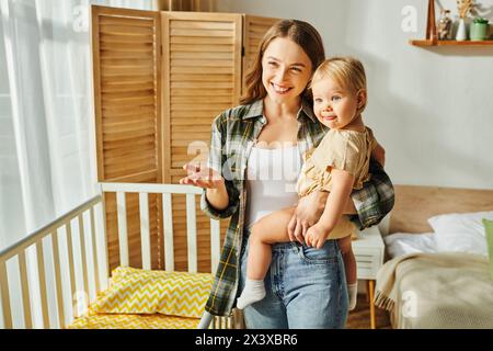 la giovane madre felice culla amorevolmente la figlia tra le braccia, creando un tenero momento di connessione e affetto a casa. Foto Stock