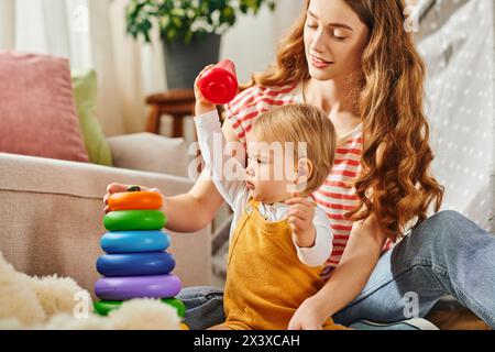 Una giovane madre si impegna gioiosamente con la figlia mentre gioca sul pavimento a casa. Foto Stock