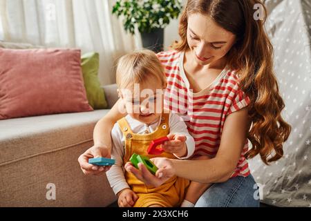 Una giovane madre interagisce felicemente con la figlia, impegnandosi in attività ludiche sul pavimento di casa. Foto Stock