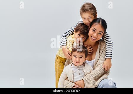 Una giovane madre asiatica e i suoi figli si mettono in posa in uno studio su uno sfondo grigio, irradiando amore e felicità. Foto Stock