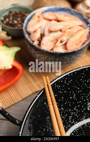 Wok nero, bacchette e tappetino in bambù con prodotti sul tavolo, primo piano Foto Stock