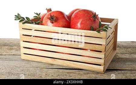 Melograni freschi e foglie verdi in scatola su un tavolo di legno su sfondo bianco Foto Stock