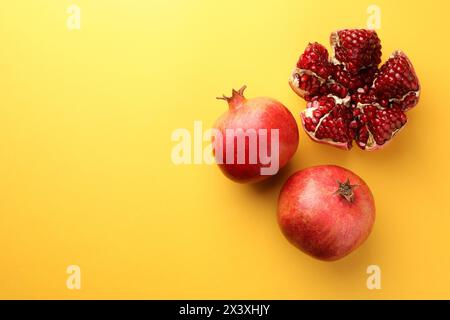 Intero e tagliare melograni freschi su sfondo giallo, piatto. Spazio per il testo Foto Stock