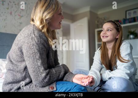 Mamma matura seduta sul letto con la figlia adolescente a casa che indossa apparecchi ortodontici che parlano e ridono Foto Stock