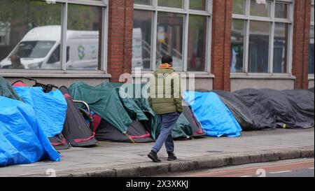 Persone che passano accanto alle tende che ospitano richiedenti asilo vicino all'Ufficio di protezione internazionale, a Dublino. Le affermazioni secondo cui la maggior parte dei richiedenti asilo che entrano in Irlanda aveva attraversato il confine dall'Irlanda del Nord sono state messe in discussione dalle organizzazioni per i diritti umani e i rifugiati. La scorsa settimana, il ministro della giustizia irlandese Helen McEntee ha affermato che il numero di richiedenti asilo che attraversano l'Irlanda del Nord verso lo Stato è ora "superiore al 80 per cento” a seguito di un cambiamento dei modelli migratori negli ultimi mesi. Data foto: Lunedì 29 aprile 2024. Foto Stock