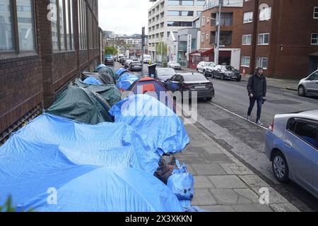 Persone che passano accanto alle tende che ospitano richiedenti asilo vicino all'Ufficio di protezione internazionale, a Dublino. Le affermazioni secondo cui la maggior parte dei richiedenti asilo che entrano in Irlanda aveva attraversato il confine dall'Irlanda del Nord sono state messe in discussione dalle organizzazioni per i diritti umani e i rifugiati. La scorsa settimana, il ministro della giustizia irlandese Helen McEntee ha affermato che il numero di richiedenti asilo che attraversano l'Irlanda del Nord verso lo Stato è ora "superiore al 80 per cento” a seguito di un cambiamento dei modelli migratori negli ultimi mesi. Data foto: Lunedì 29 aprile 2024. Foto Stock