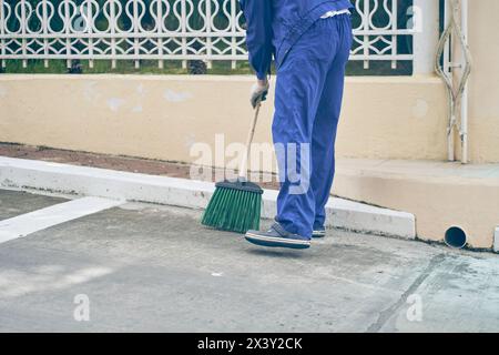 Il custode spazza il parcheggio accanto al negozio con una scopa. Pulire la città, le strade da polvere e sporcizia. Foto di alta qualità Foto Stock