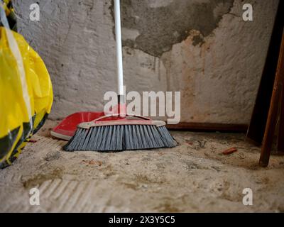 Scopa con paletta appoggiata contro la parete di cemento in un cantiere. Pulizia dei pavimenti dopo i lavori di ristrutturazione della casa. Foto Stock
