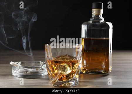 Dipendenza da alcol. Whisky in vetro, bottiglia, sigarette e posacenere su un tavolo di legno Foto Stock