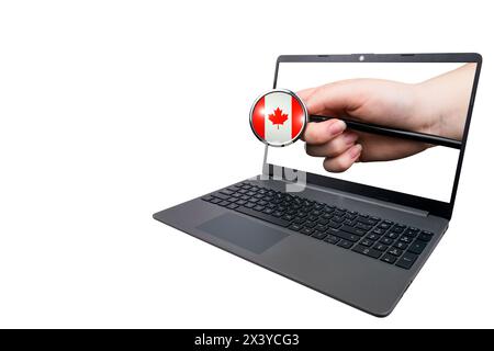 La mano con uno stetoscopio con una testa a forma di bandiera canadese si stacca da un computer portatile su uno sfondo bianco. Il concetto di sistema sanitario canadese Foto Stock