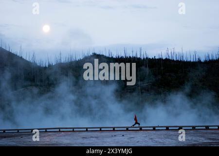 Una donna pratica yoga all'alba mentre il vapore proveniente dalla Grand Prismatic Spring la avvolge nel parco nazionale di Yellowstone, Wyoming. Foto Stock