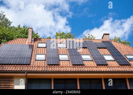 I pannelli solari rivestono il tetto di una casa suburbana, una testimonianza delle tendenze della vita sostenibile e delle energie rinnovabili, sotto un cielo azzurro. Pol. Di alta qualità Foto Stock
