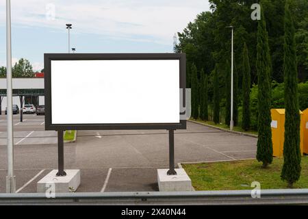 In una giornata di sole, un grande cartello bianco si trova in primo piano nel mezzo di un parcheggio vuoto. Foto Stock