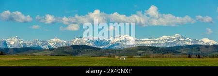 Splendida vista panoramica delle Montagne Rocciose canadesi con il suo crinale leggermente innevato con colline ondulate, cielo blu e nuvole bianche e soffici Foto Stock