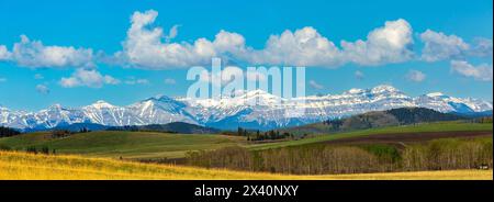 Splendida vista panoramica delle Montagne Rocciose canadesi con il suo crinale leggermente innevato con colline ondulate, cielo blu e nuvole bianche e soffici Foto Stock