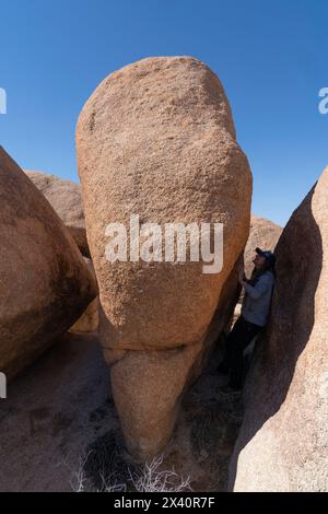 Donna in piedi in un punto stretto tra grandi rocce, esplorando le splendide formazioni rocciose del Joshua Tree National Park Foto Stock