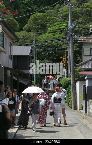 Vita quotidiana in Giappone Una scena estiva di avvicinamento al santuario Kamakura Goryo, dove le donne in yukata e le persone con ombrelloni vanno e vengono Foto Stock