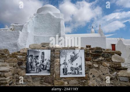 Fotografie storiche in bianco e nero montate su un muro di pietra a Mykonos, con una chiesa bianca sullo sfondo; Mykonos, Egeo meridionale, Grecia Foto Stock