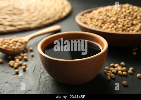 Gustosa salsa di soia nel recipiente e semi di soia sul tavolo nero, primo piano Foto Stock