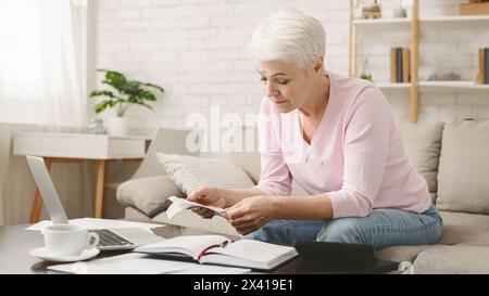 Donna anziana che esamina documenti finanziari a casa in giorno Foto Stock