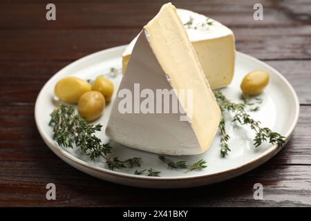 Piatto con pezzi di gustoso formaggio camembert, olive e rosmarino su tavola di legno, primo piano Foto Stock