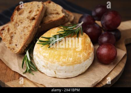 Gustoso camembert al forno, pezzi di pane, uva e rosmarino in tavola, primo piano Foto Stock