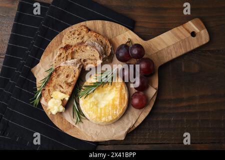 Gustoso camembert al forno, pezzi di pane, uva e rosmarino su un tavolo di legno, vista dall'alto Foto Stock