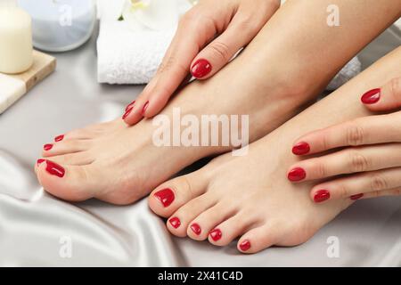 Donna con eleganti unghie rosse dopo la procedura di pedicure su tessuto di seta grigia, primo piano Foto Stock