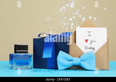 Buona festa del papà. Biglietto con la frase i Love You, papà in busta, papillon, profumo e confezione regalo su tavolo azzurro, primo piano Foto Stock