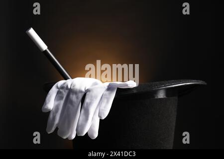 Cappello da mago, guanti e bacchetta su sfondo scuro, primo piano Foto Stock