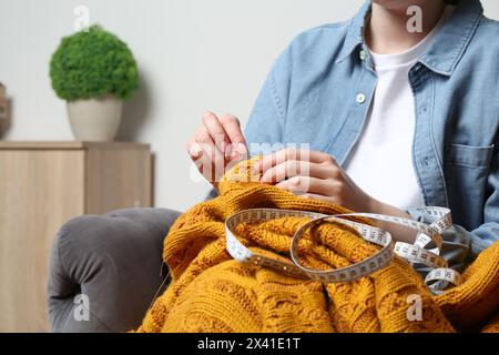 Donna che cucisce maglione con ago a casa, primo piano Foto Stock