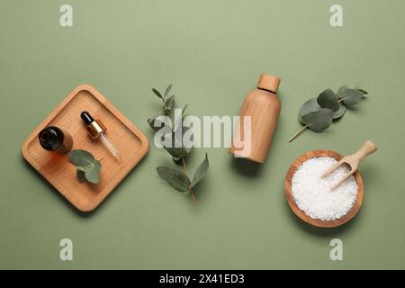 Prodotti aromaterapici. Bottiglie di olio essenziale, sale marino e foglie di eucalipto su fondo di oliva, pianeggianti Foto Stock