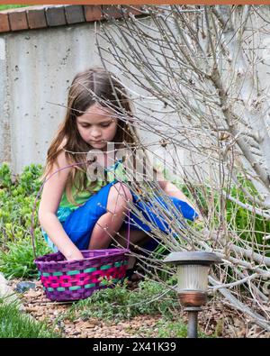 Una ragazza caucasica di sei anni guarda le uova che ha raccolto durante una caccia all'uovo di Pasqua. STATI UNITI. Foto Stock