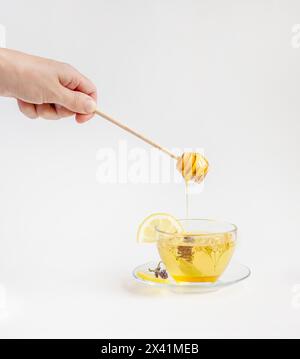 Fai gocciolare il miele su una tazza di tè alle erbe circondato da fiori e bottiglie. Concetto di stile di vita sano e rimedi naturali Foto Stock